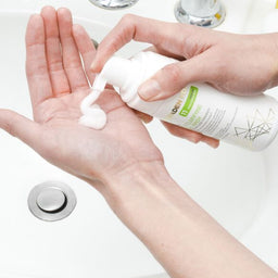 Person applying a white cream from a bottle labeled 'IDENTITY' on their palm.