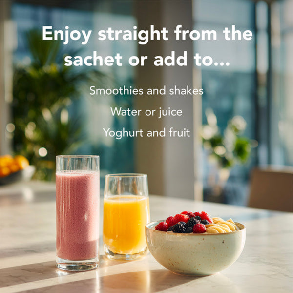 Two glasses of smoothies and a bowl of fruit on a table with a blurred outdoor background.