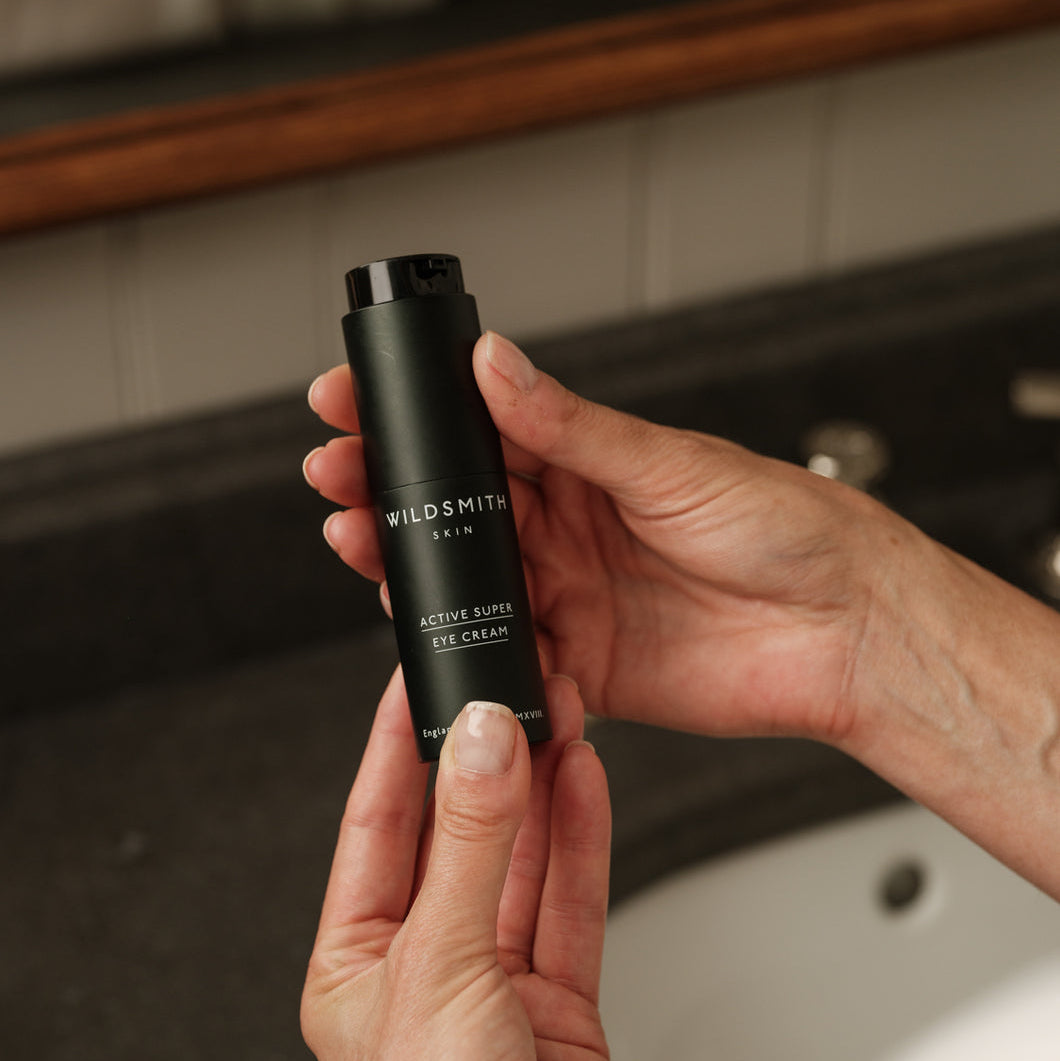 Hand holding a black skincare product labeled 'Wildsmith' in a bathroom setting.