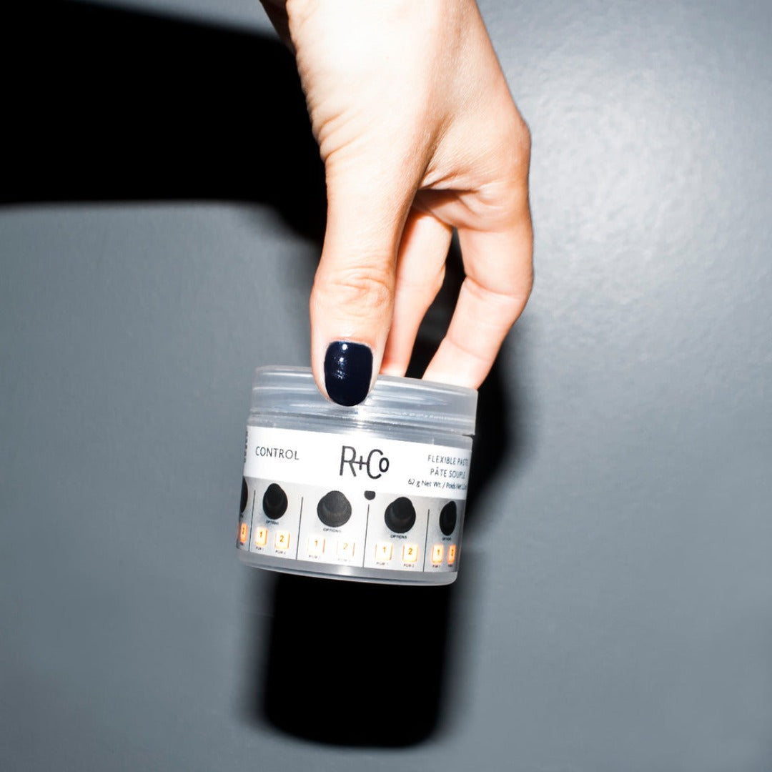 a tub of R+Co Control Flexible Paste held in the air