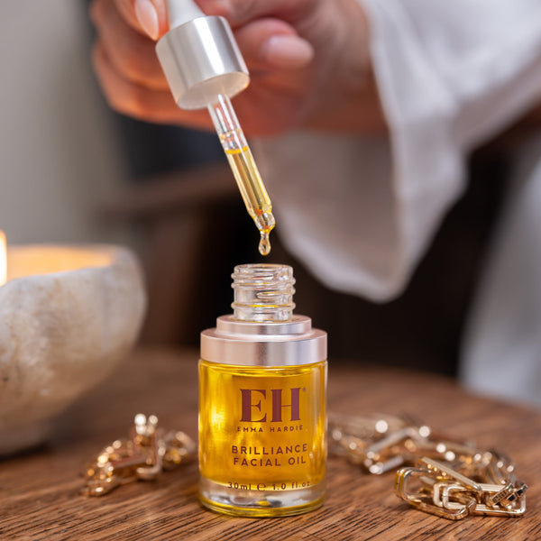 Hand using a dropper to add oil from a bottle labeled 'EH' onto a wooden surface.