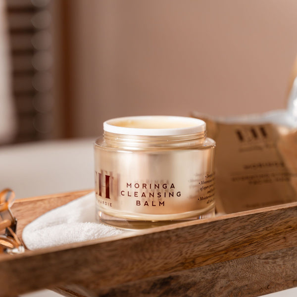 Jar of Moringa Cleansing Balm on a wooden tray with a blurred background