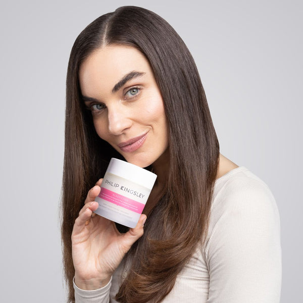 Woman holding a Philip Kingsley skincare product against a gray background