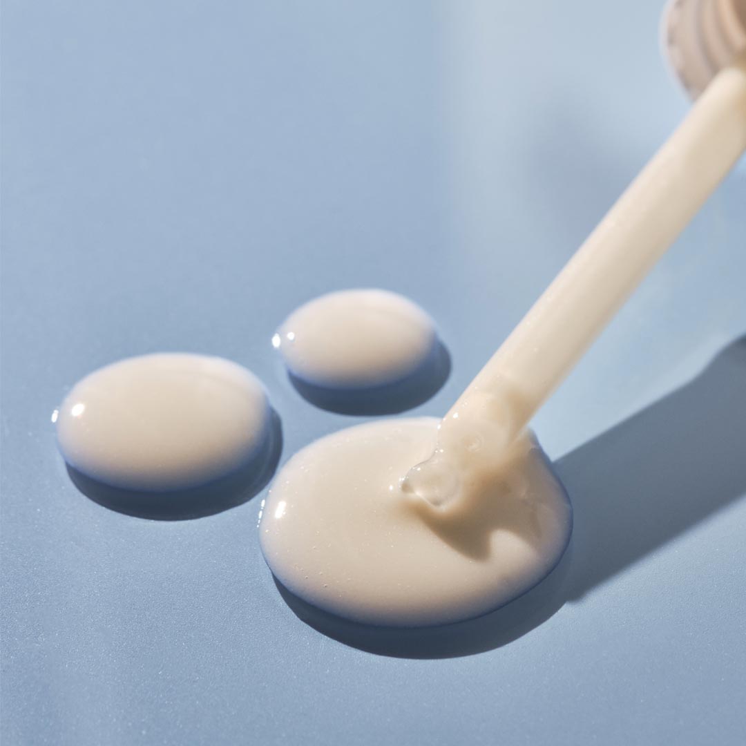 Close-up of a dropper dispensing cream onto a light blue background