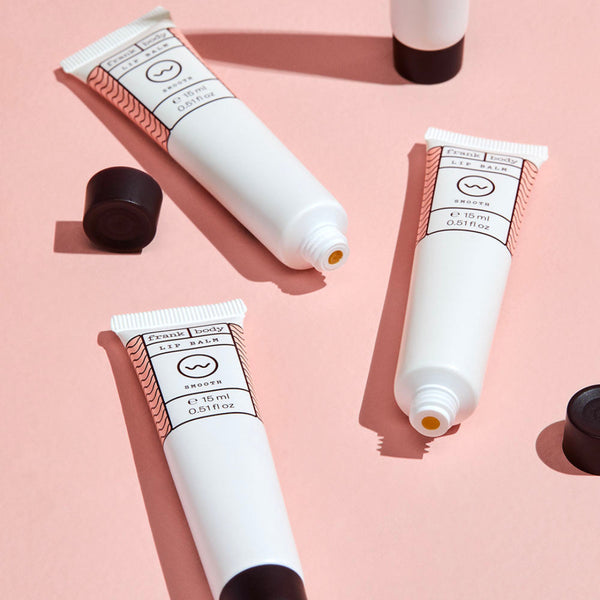 Three white lip balm tubes with black caps on a pink background