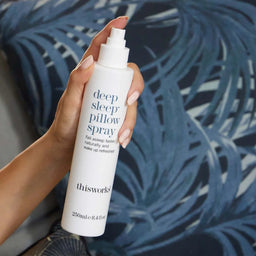 Hand holding a bottle of 'deep sleep pillow spray' with a blue leafy background