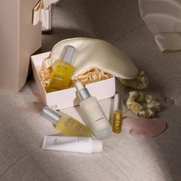 A spa gift set featuring multiple ESPA skincare products including a sleep mask, serum, toner, cream, and rollerball, arranged on a textured beige fabric surface next to a gift box.