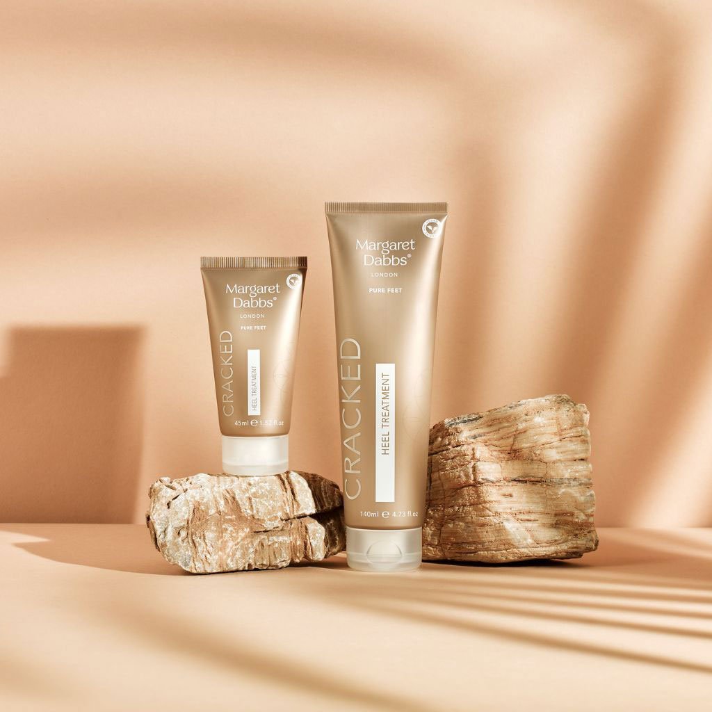 Two tubes of Margaret Dabbs Cracked heel treatment on a beige background with stone-like textures.